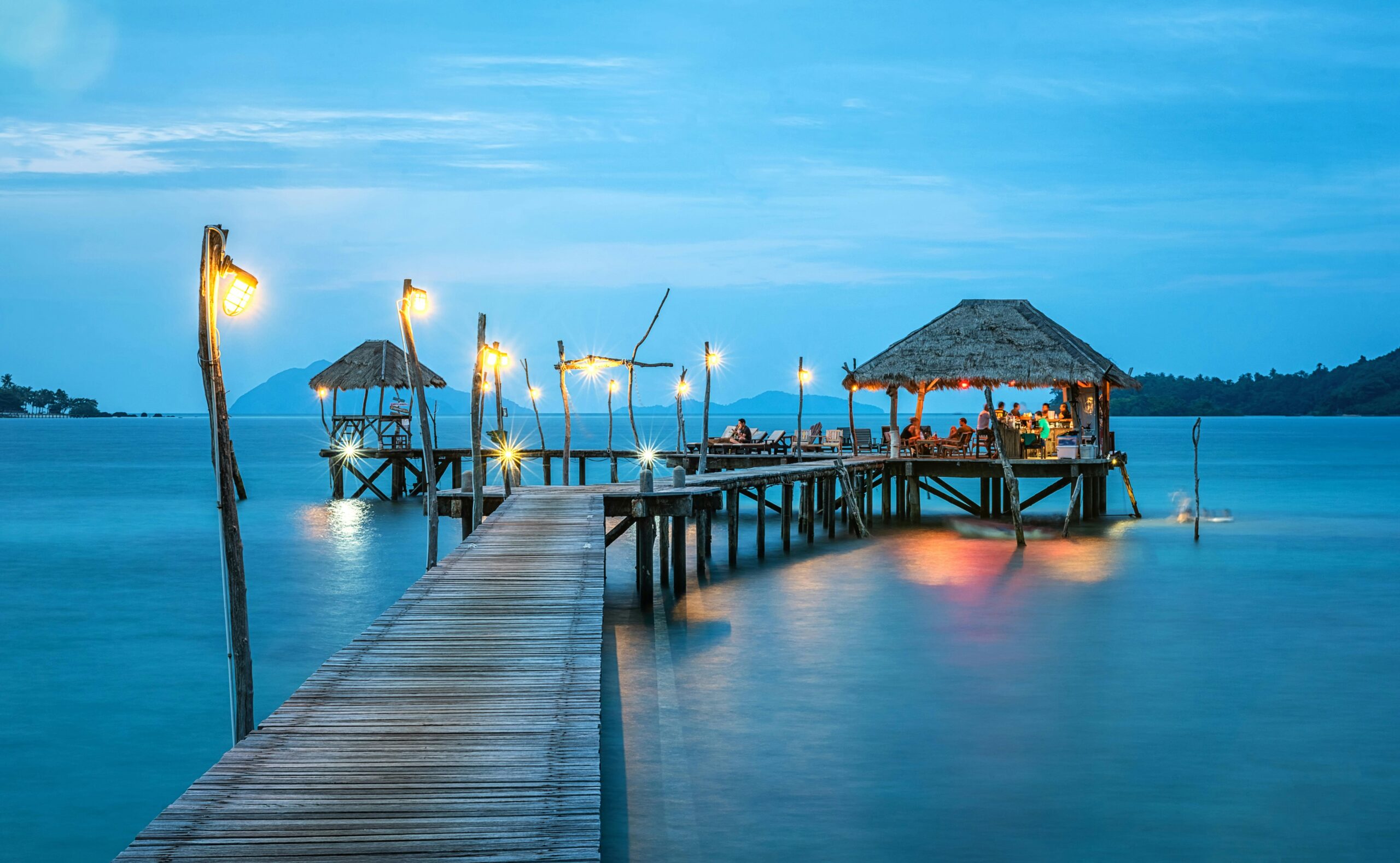 Illuminated pier and bungalow on a tranquil tropical sea at twilight.