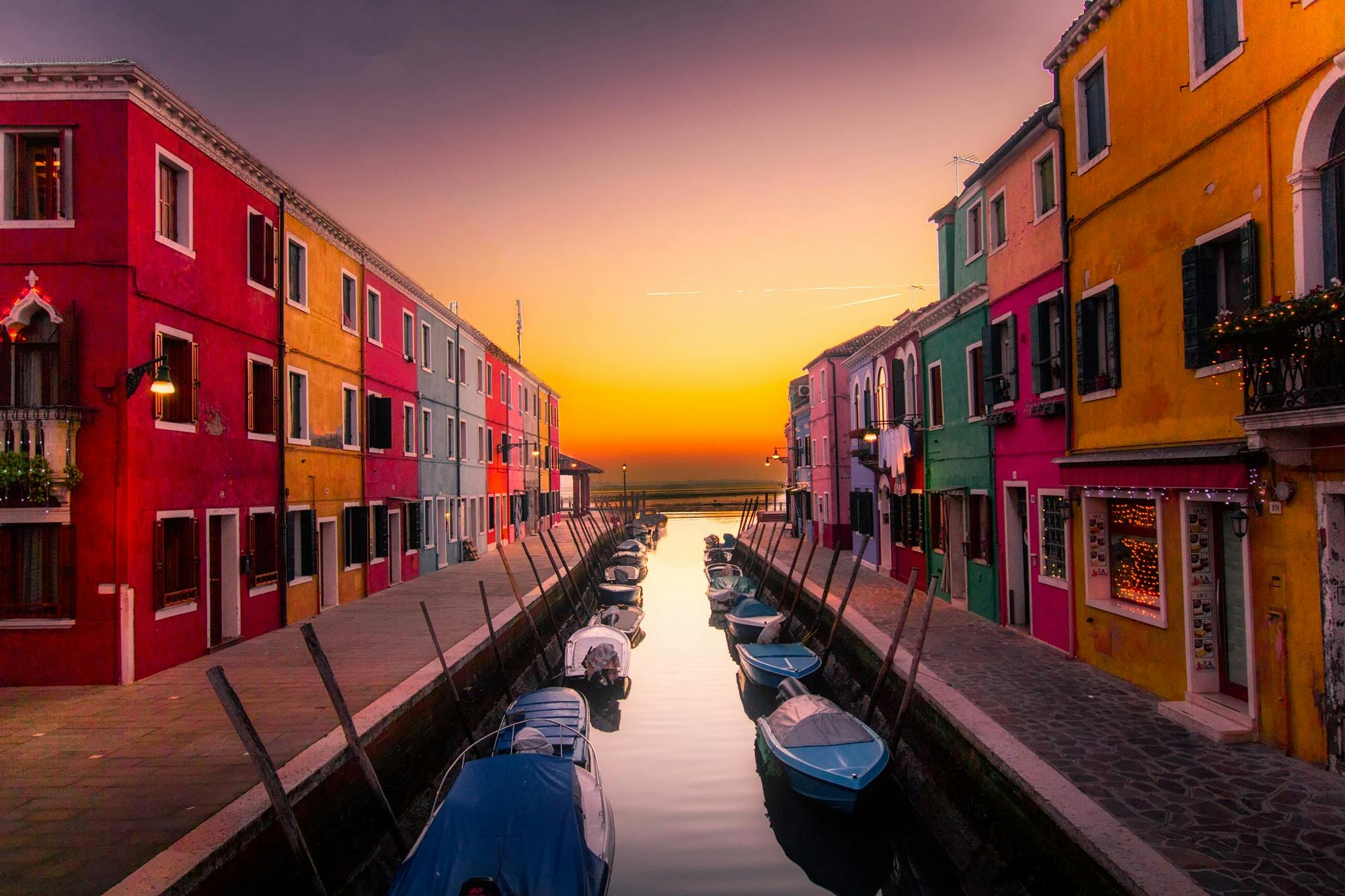 Vibrant facades along Burano's canal with boats at serene sunset. Perfect travel snapshot.