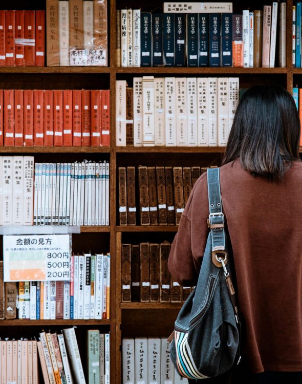 Woman Wearing Brown Shirt Carrying Black Leather Bag on Front of Library Books