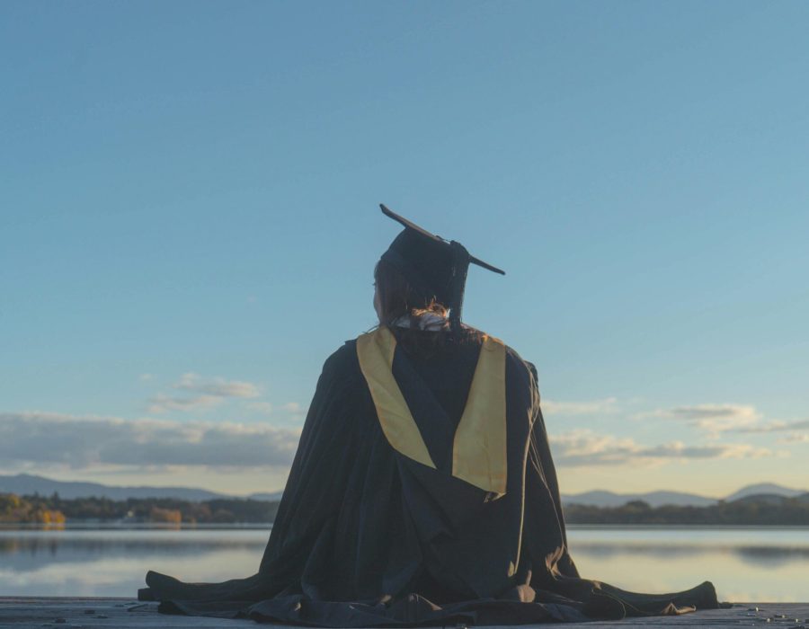 Back View of a Student Wearing a Graduation Gown and a Mortarboard, Sitting by a Lake